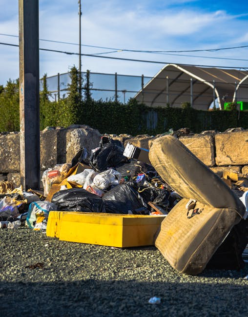 Close-up view of a rocky shoreline with various types of litter scattered along the edge where the land meets the water. The debris includes plastic bottles in green, clear, and brown, some crushed or